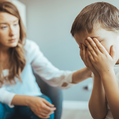 Little boy with hands covering face while mother comforts him, representing dental anxiety in children