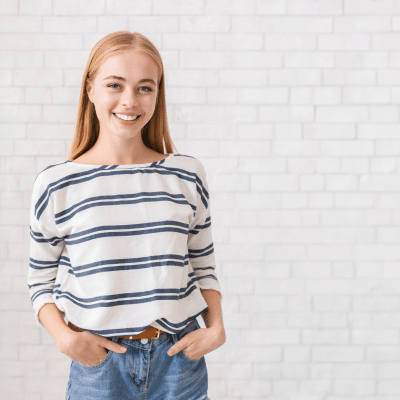 Teenage girl standing and smiling with hands in her pants pocket, representing healthy smiles